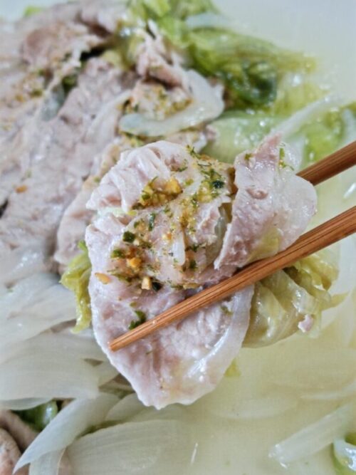 お箸で七味がかかった蒸し料理（豚肉、レタス）を掴む様子。