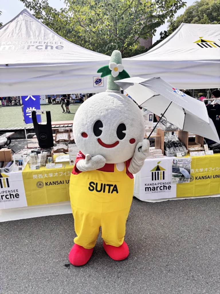 吹田市キャラクターのすいたんが傘を片手に、もう片手を口元に添えてかわいくポーズしている様子。