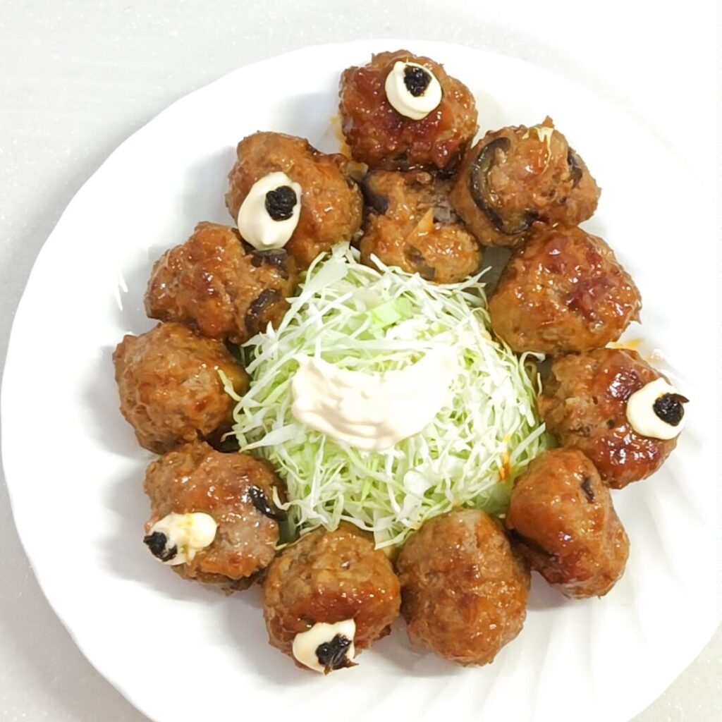 自宅で手作りしたミートボールに一部マヨネーズと海苔の佃煮で目玉を描き、真ん中にはキャベツの千切り、その上にマヨネーズで口を描き、大阪・関西万博公式キャラクターのミャクミャク風にお皿に盛り付けた写真