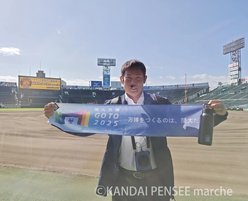 ※甲子園球場での関西大学千寿会イベントにて（2024年秋撮影）、関大OB、元阪神タイガース投手の岩田稔さんに「カイザーズグッズ/真空ステンレス炭酸ボトル」「カイザーズグッズ／ゴルフマーカー」「関大万博オフィシャルグッズ／マフラータオル」を持っていただいた写真