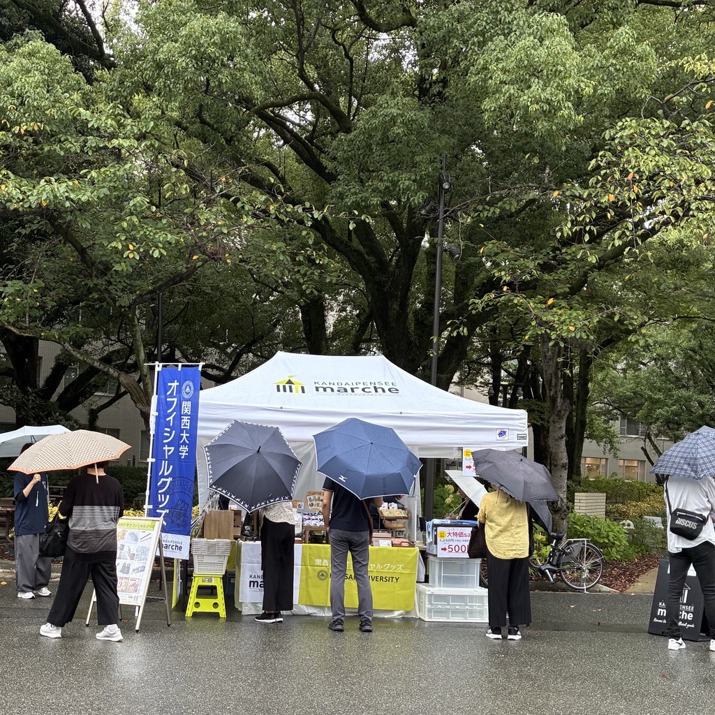 傘をさしてカンダイパンセマルシェの商品を見る人々