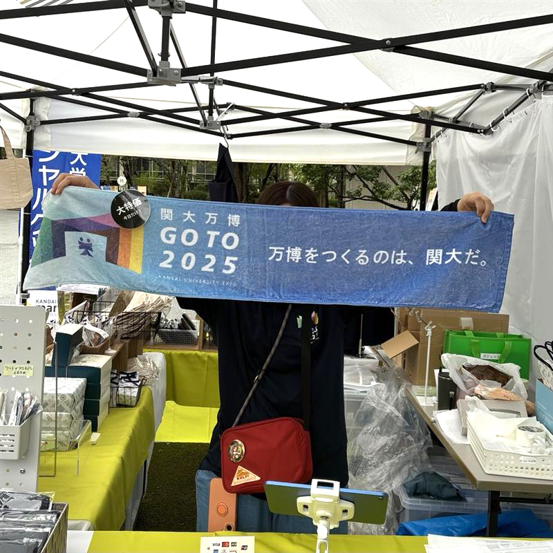 関大万博マフラータオルを顔の前に掲げるスタッフ