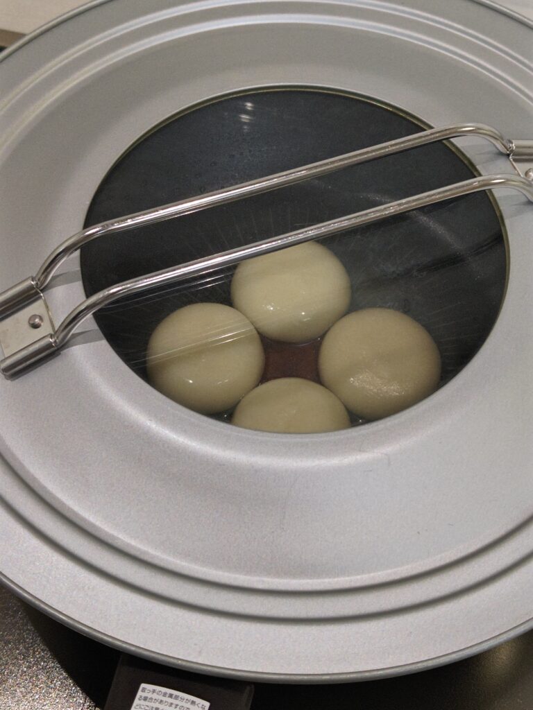 フライパンに丸もちを４つ並べています。丸もちは、地域特産「紅せんり」ブランド。丹波青垣産の滋賀羽二重もち使用「紅せんりのおもち」。もちピザを作るために、フタをして蒸し焼きしています。