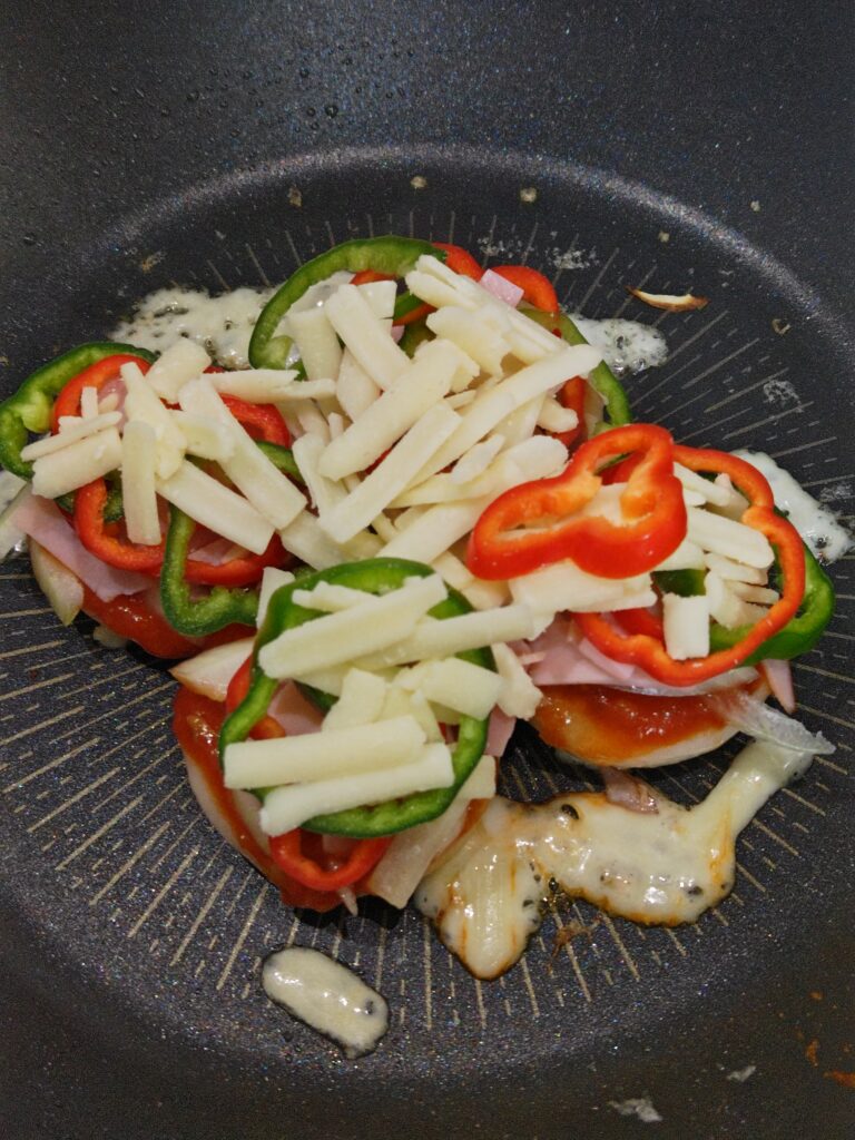 蒸し焼きした丸もち４つの上に、ピザのトッピングをのせています。ピザソースを塗り、うすくスライスした玉ねぎ、輪切りのピーマン、ベーコン、とろけるチーズをのせています。