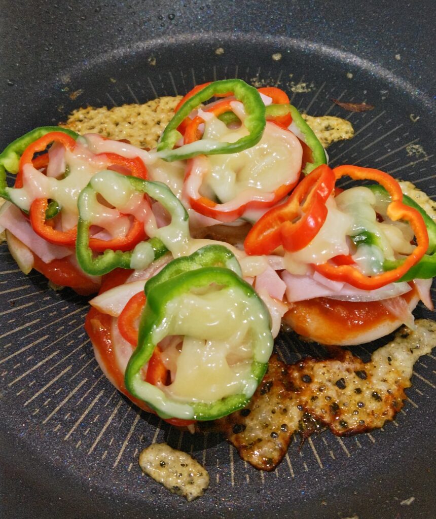 蒸し焼きした丸もち４つの上に、ピザのトッピングをのせてさらに蒸し焼きしました。ピザソース、うすくスライスした玉ねぎ、輪切りのピーマン、ベーコン、とろけるチーズをのっています。