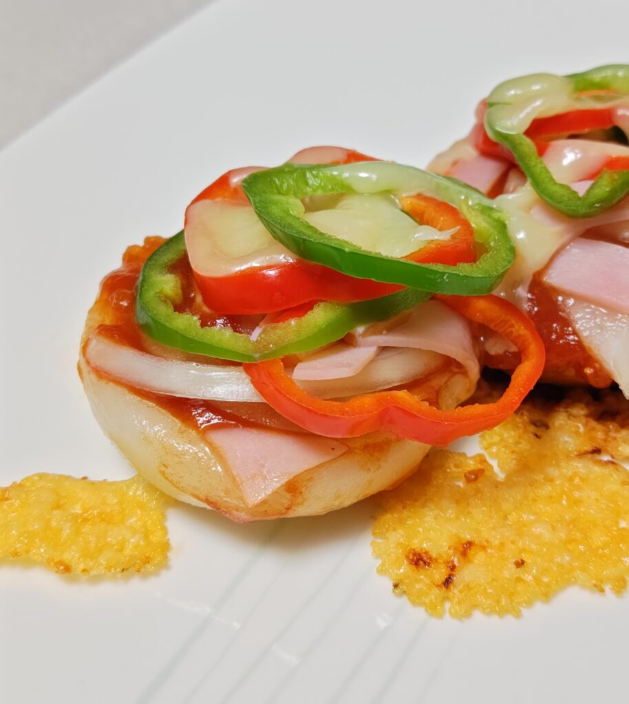 蒸し焼きしたもちピザの出来上がり。白いお皿の上にのせています。とろけ流れたチーズが少しこんがり平たく乗っています。