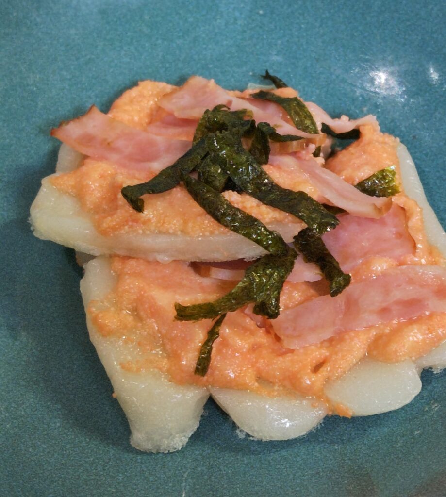 フライパンで蒸し焼きしたおもちピザを、青い和食器に盛り付けています。おもちピザのトッピングは、たらこマヨ、ベーコン、海苔です。