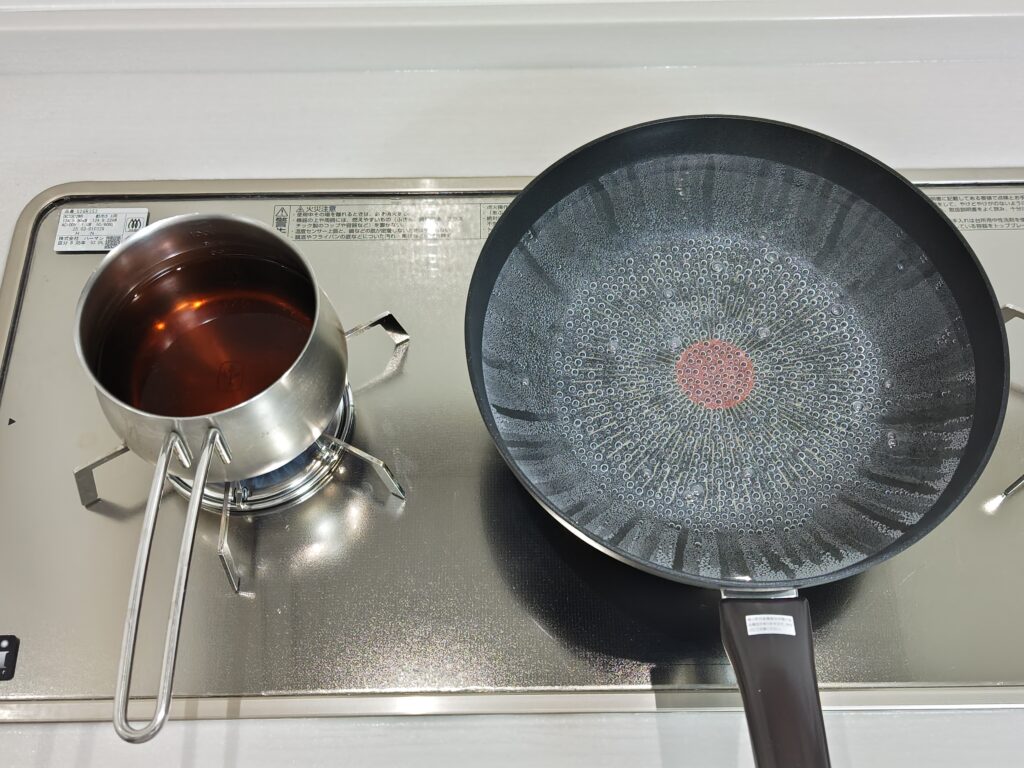 ガスコンロの上に、お蕎麦を茹でる用の深めのフライパンに2リットルのお湯がグツグツ湧いています。左隣の小鍋に、そばつゆを沸かしています。