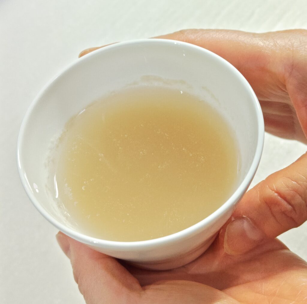 白い器に、関西大学と企業の産学連携で誕生した「九・九割蕎麦」の茹で汁に、そばつゆを加えた蕎麦湯を両手で持っています