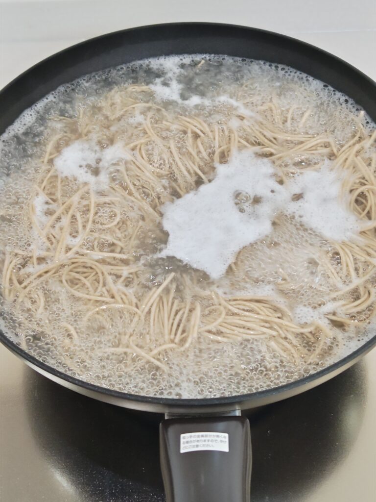 ガスコンロの上に、たっぷりのお湯が沸いている深めのフライパンに、お蕎麦が茹でられています。