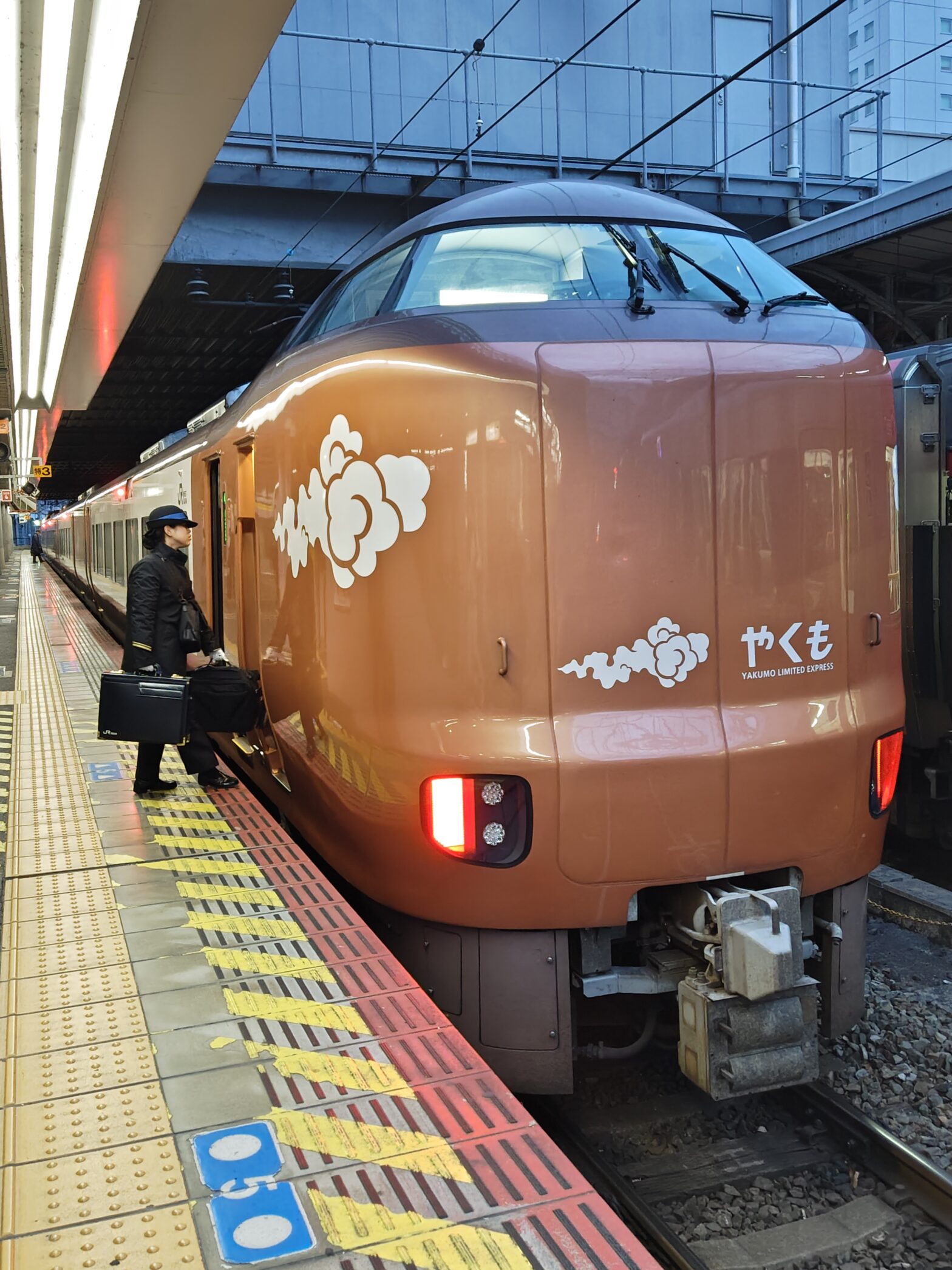 岡山駅に停車中の新型特急やくも273系「やくもブロンズ」正面写真。車掌さんが四角い黒いカバンを持って乗り込もうとする姿